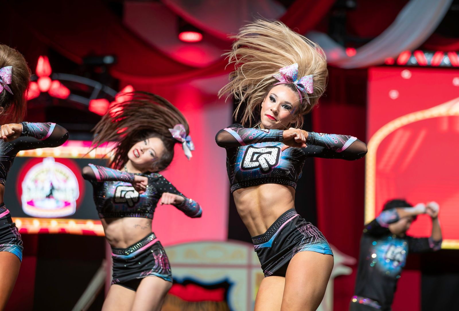Cheer athletes mid-routine with hair flying under red stage lights