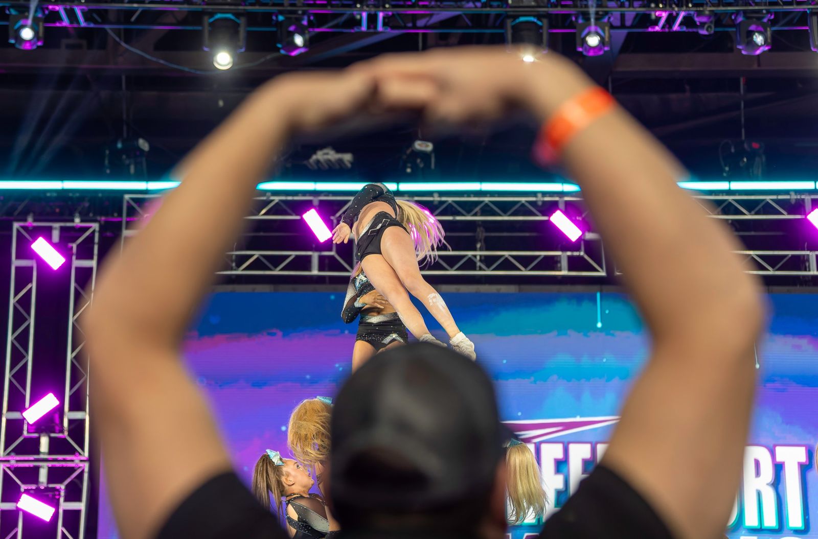 A fan making a heart with their hands, framing a stunt on stage